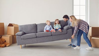 Vater und Mutter heben die Couch mit ihren 2 Kindern drauf
