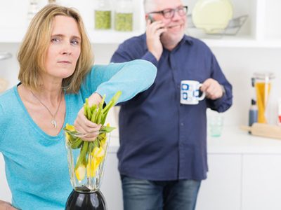Frau ärgert sich und schlendert Blumen von Ihrem Mann während dieser telefoniert und nichts merkt.