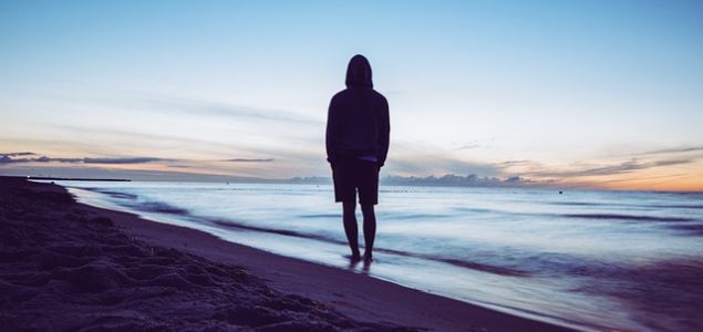 Eine Person steht am Strand und blickt aufs Meer.