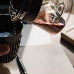 Eine Person gießt am Schreibtisch Kaffee in eine Tasse.