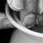 Hände formen ein Tongefäß auf einer Töpferscheibe.