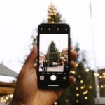 Mit einem Smartphone wird der Weihnachtsbaum auf einem Weihnachtsmarkt fotografiert.