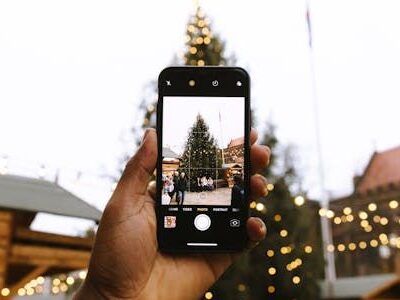 Mit einem Smartphone wird der Weihnachtsbaum auf einem Weihnachtsmarkt fotografiert.
