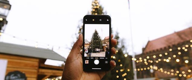Mit einem Smartphone wird der Weihnachtsbaum auf einem Weihnachtsmarkt fotografiert.