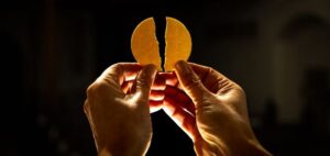 Zwei Hände halten eine gebrochene Hostie.