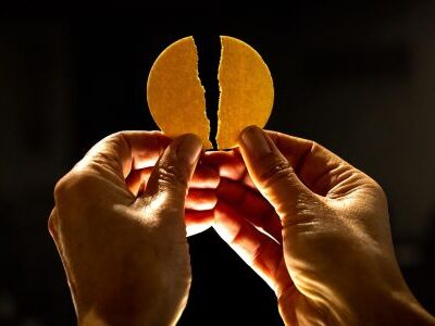 Zwei Hände halten eine gebrochene Hostie.