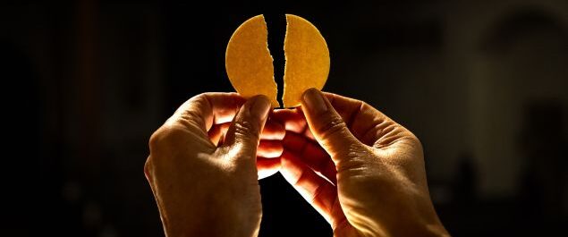 Zwei Hände halten eine gebrochene Hostie.