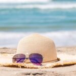 Ein Sonnenhut und eine Sonnenbrille liegen im Sand eines Strandes.