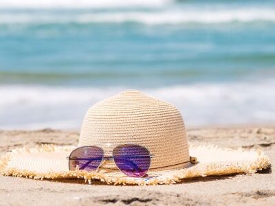 Ein Sonnenhut und eine Sonnenbrille liegen im Sand eines Strandes.