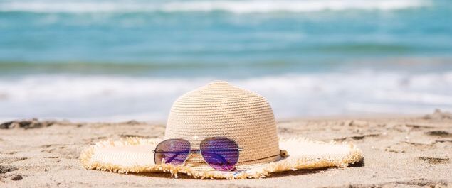 Ein Sonnenhut und eine Sonnenbrille liegen im Sand eines Strandes.