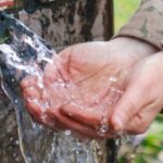Zu einer Schale geformte Hände empfangen Wasser aus einer Quelle.