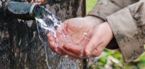 Zu einer Schale geformte Hände empfangen Wasser aus einer Quelle.