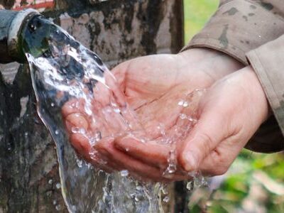 Zu einer Schale geformte Hände empfangen Wasser aus einer Quelle.