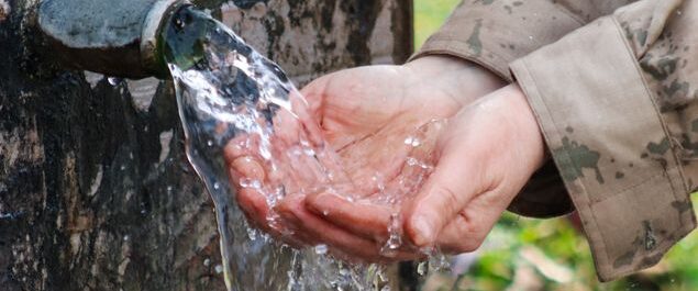 Zu einer Schale geformte Hände empfangen Wasser aus einer Quelle.